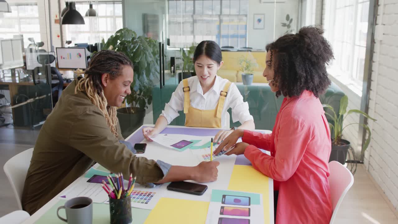 Busy diverse diverse designers at table discussing work in casual office meeting, in slow motion
