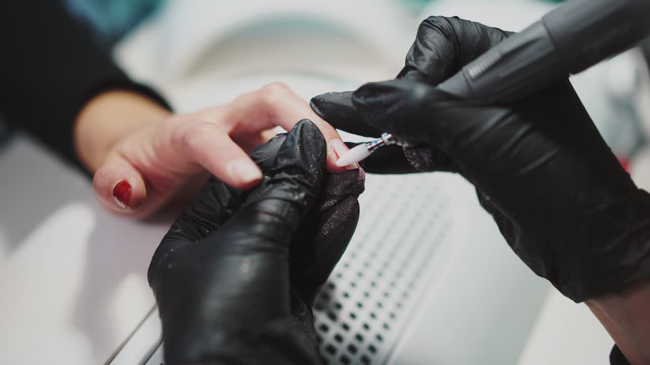 master of manicure is holding the client's hand and removing the gel polish by professional equipment in the beauty salon