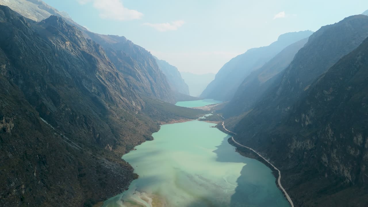 A breathtaking high-altitude aerial flyover through a dramatic U-shaped glacial valley above the turquoise Llanganuco Lakes in Peru's Cordillera Blanca