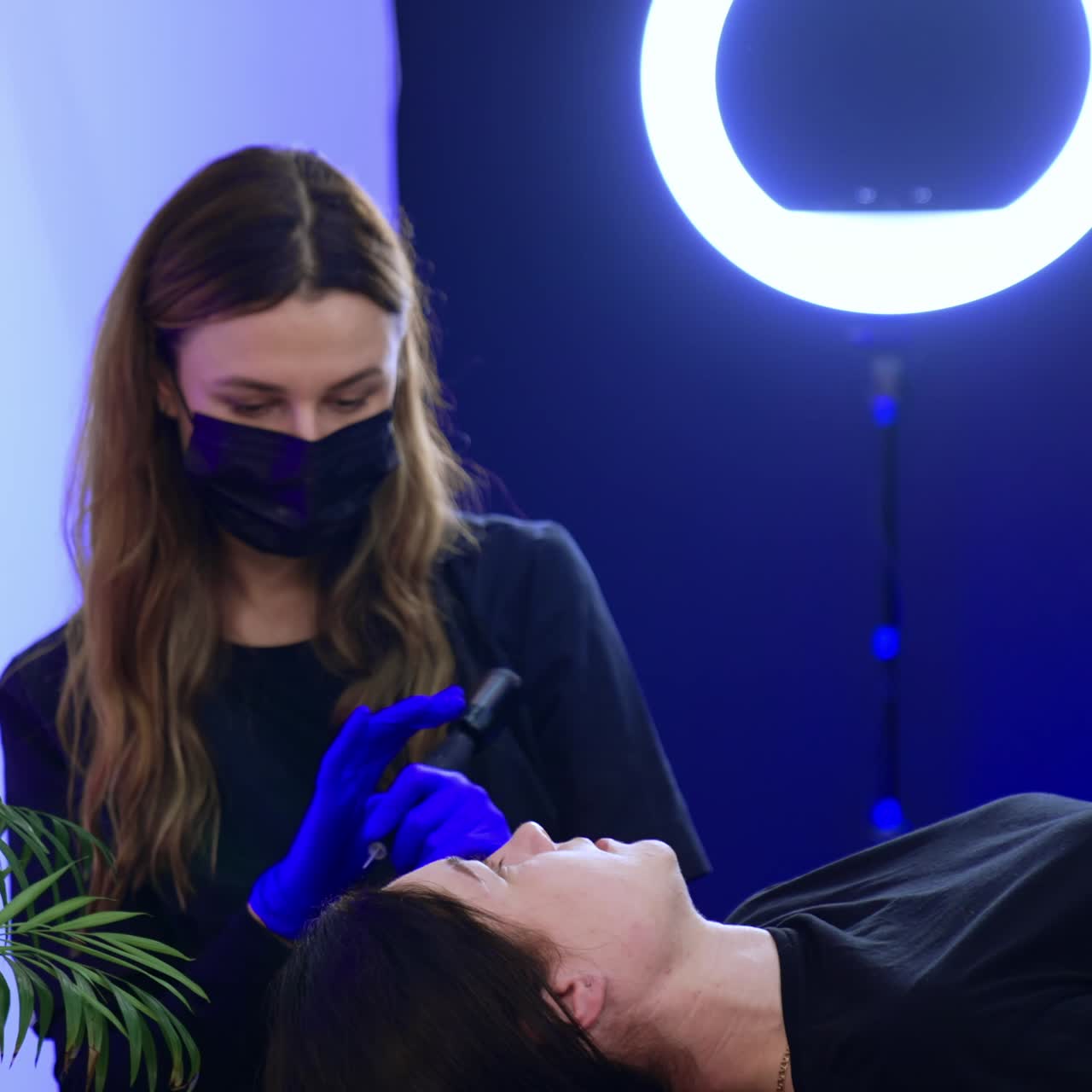 Caucasian cosmetologist wearing black mask working in a beauty salon. Specialist performing permanent eyebrow make up