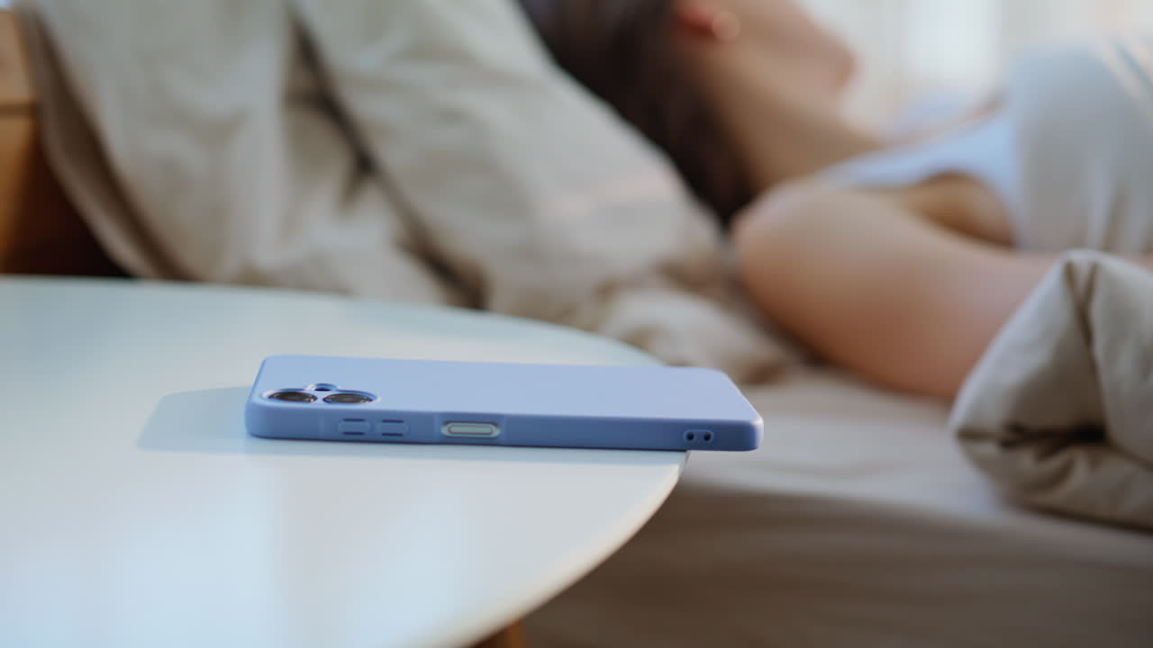 Primo piano di una donna che spegne la sveglia sullo smartphone al mattino in una camera da letto luminosa