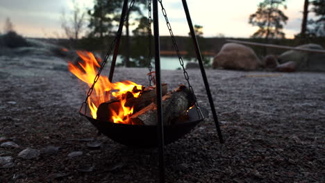 metal fire place burning in front of stones and lake, wooden campfire