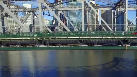 toma aérea del story bridge al nivel de la carretera, mientras el dron se mueve junto con el tráfico y el distrito ribereño de brisbane se puede ver al fondo.