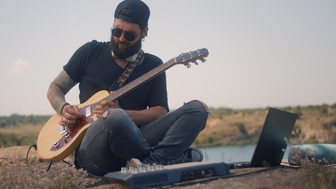 Musician Playing Guitar Outdoors with Laptop and Audio Equipment