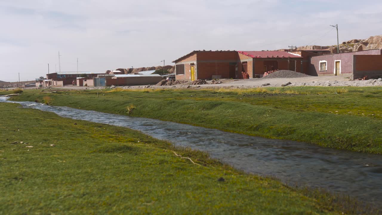 pueblo rural boliviano con arroyo y hierba verde vibrante, bajo cielos despejados, ambiente tranquilo