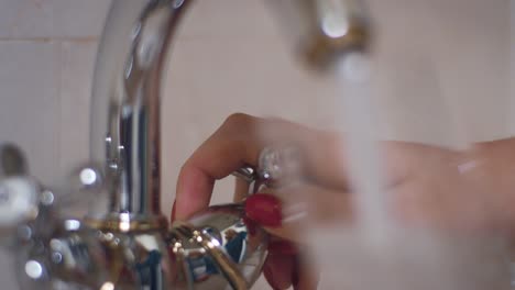 Female-hand-turning-knob-on-tap-and-pouring-water-into-glass-in-bath-room