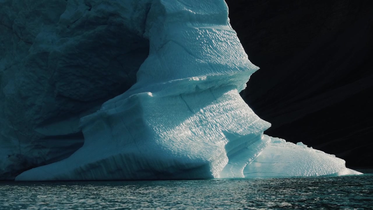 Vista ravvicinata di ghiaccio scolpito di iceberg blu che brilla sopra le scure acque dell'Oceano Artico.