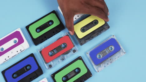 video of african american man's hand arranging retro tapes with copy space on blue background