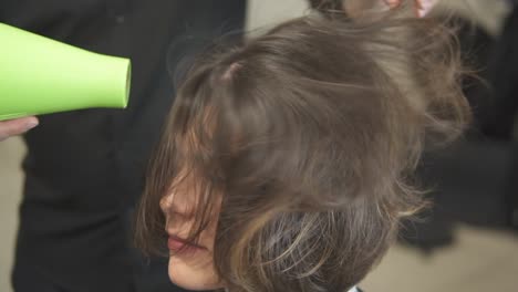 professional hairdresser using a hairdryer after haircut. young woman in beauty salon