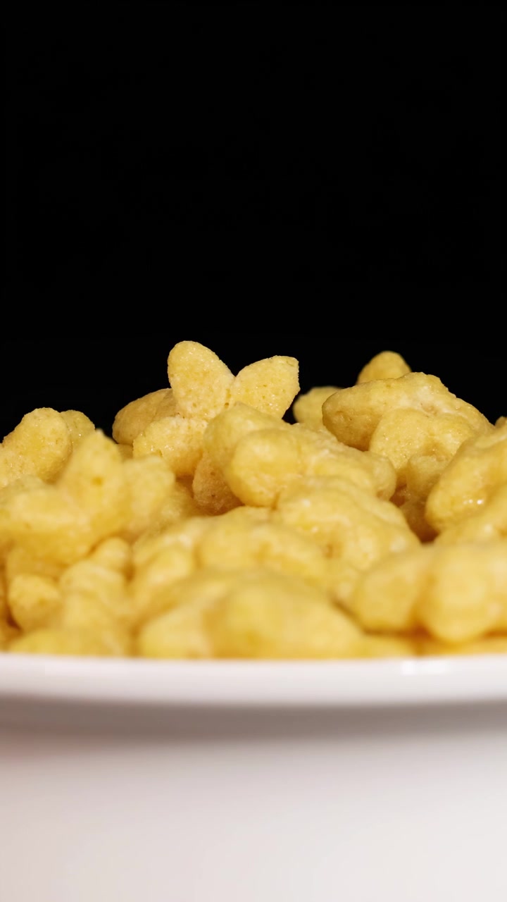 Pedaços de cereal em forma de estrela caem em uma tigela branca, em contraste com um fundo preto, criando uma cena dinâmica e divertida.
