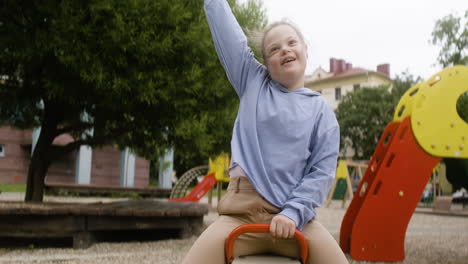 portrait of a little girl with down syndrome swinging on a wooden rocker in the park on a windy day