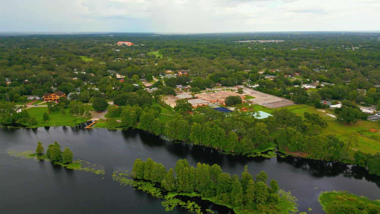 Drone slowly flying over the Hillsborough River towards a residential neighborhood school building in Tampa, Florida