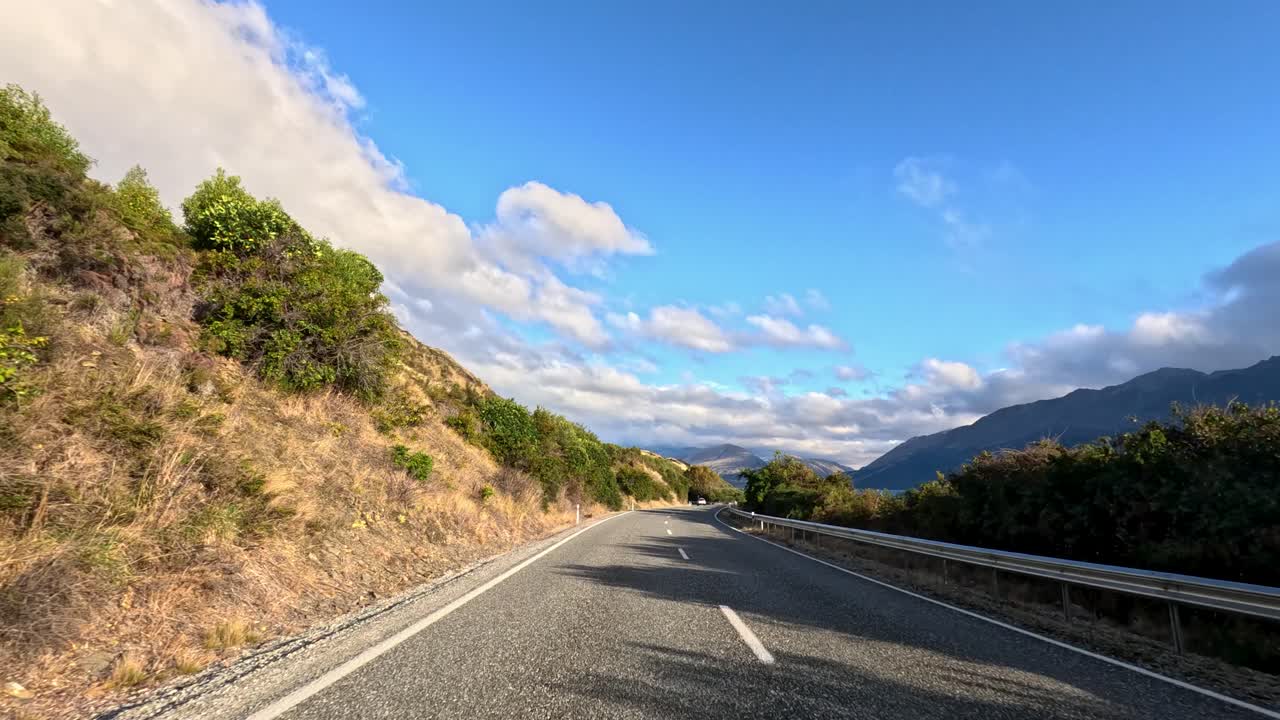 Car travels winding lakeside highway, mountain landscape, bright daylight, smooth camera movement, clear blue sky