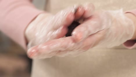 close-up demonstration video of female hands in culinary gloves holding a piece of chocolate dough and kneading a candy to make a desirable shape