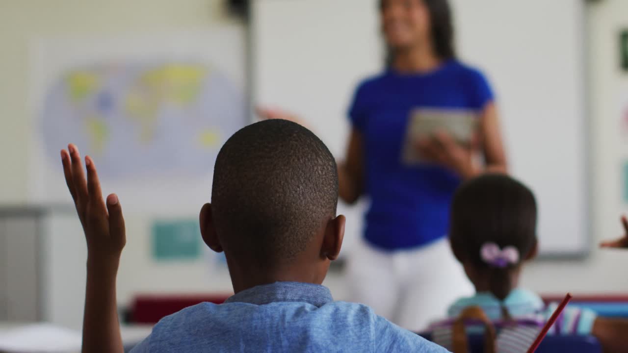 African american boy sitting in classroom raising hand to answer questions during lesson