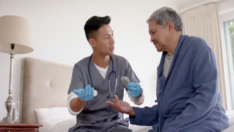 diverse male doctor testing blood of senior male patient in bed at home, slow motion