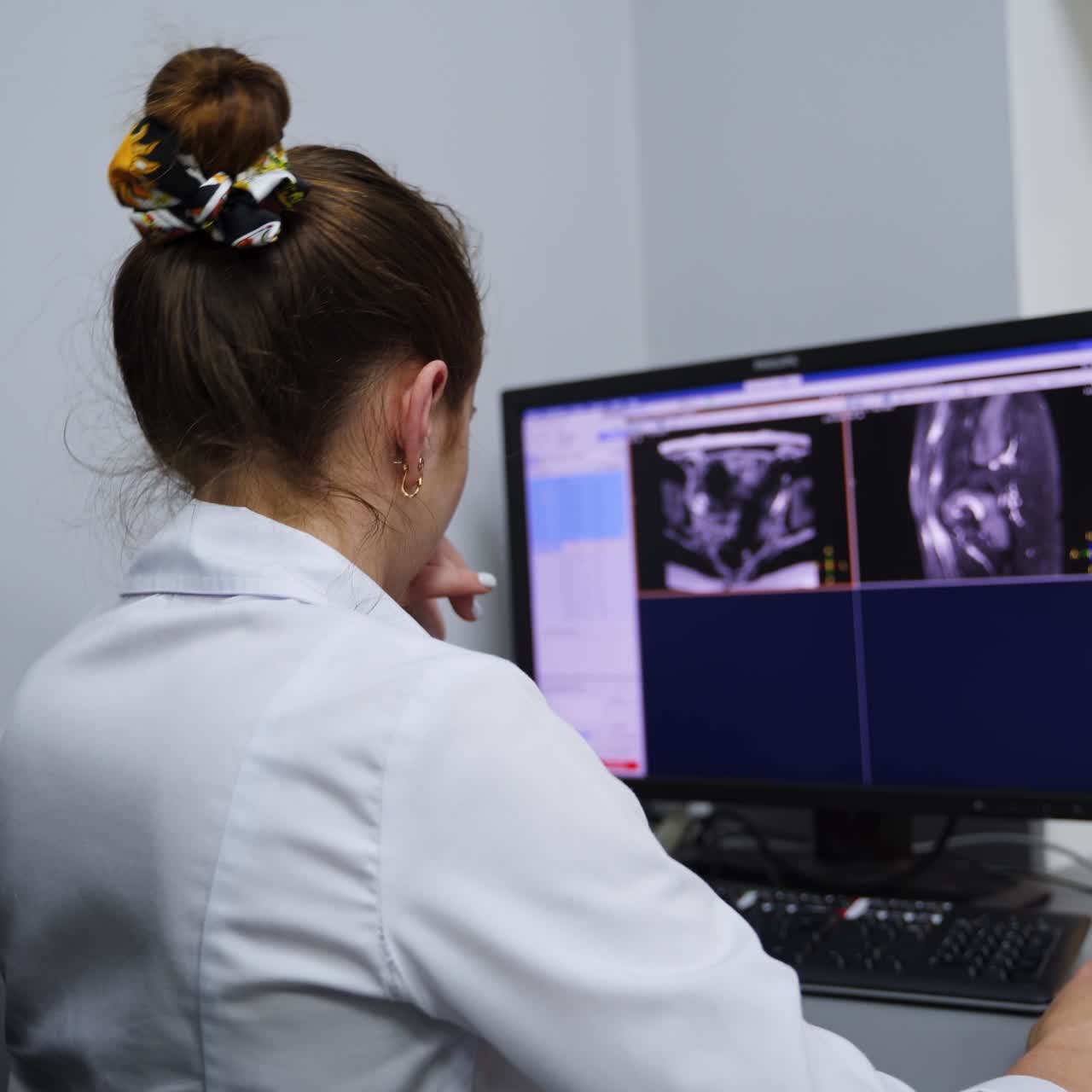 Tecnica di laboratorio seduta di spalle rivolta verso lo schermo del computer. Esperta che analizza le scansioni di risonanza magnetica di un paziente