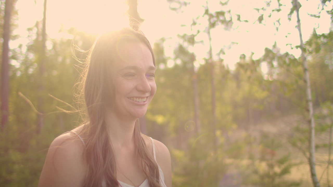 A cute girl looks into the camera and smiles in the woods in the sunny sunset rays