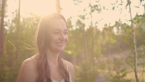 a cute girl looks into the camera and smiles in the woods in the sunny sunset rays