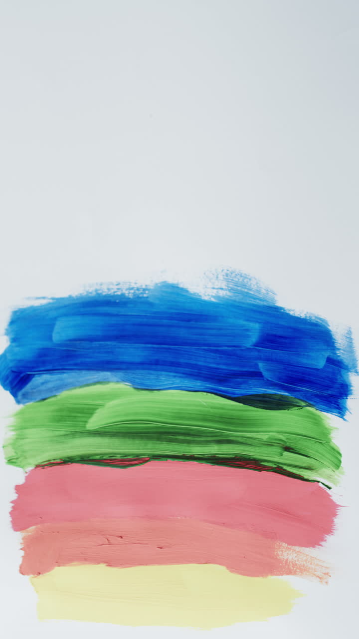 Vertical video of multi coloured paint stripes on white background with copy space, slow motion