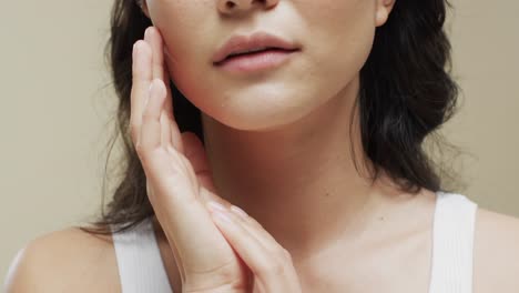 asian woman with dark hair touching her face on beige background, slow motion