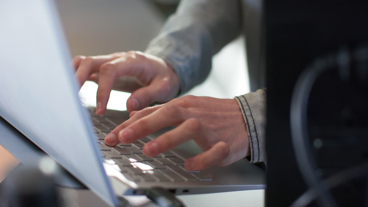 Hands settling on laptop keyboard at desk are typing code steadily for completing project at work