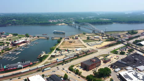 Vista-Aérea-Siguiendo-Un-Barco-Fluvial-Que-Sale-De-La-Ciudad-De-Dubuque-En-El-Río-Mississippi,-En-La-Soleada-Iowa,-EE.UU.