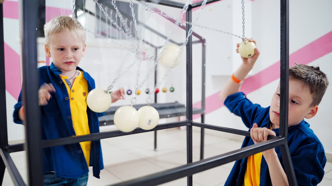Boys doing experiment with Newton's cradle physics concept for education. Museum of Science