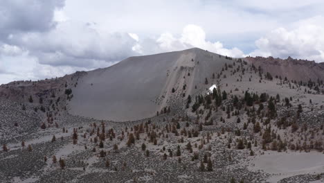 crater mountain and aeolian buttes with sparse trees under cloudy sky, aerial view