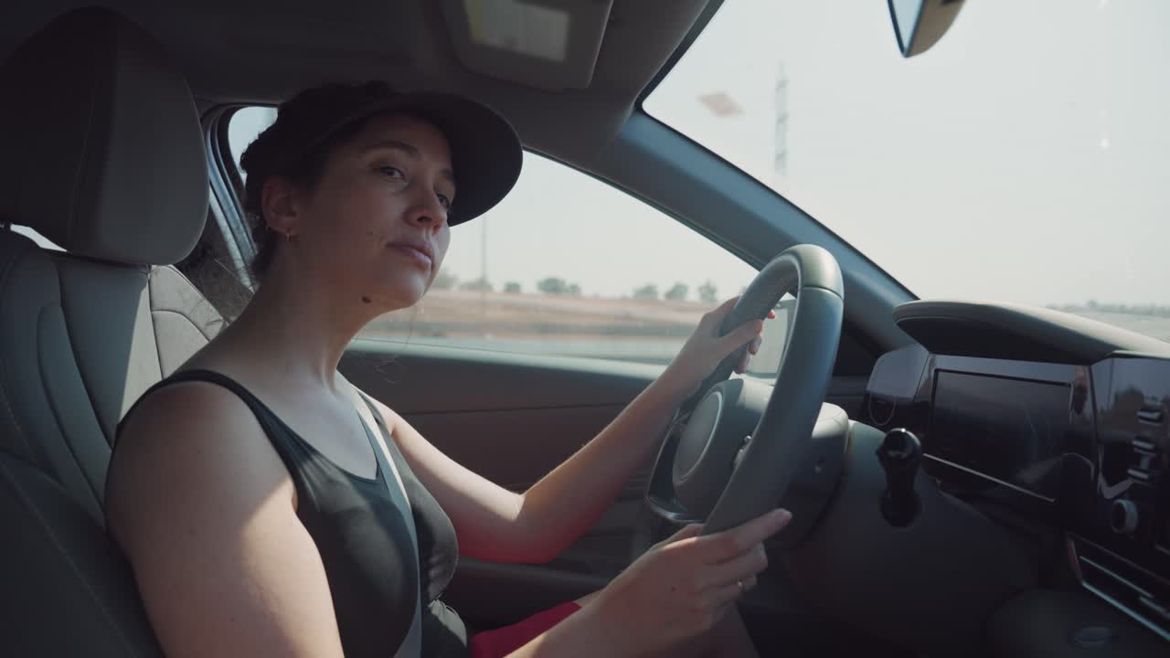 Young woman peacefully driving on highway with sedan vehicle or car looking at the road. Commute to work or enjoys leaving for vacation. Electric hybrid modern car. Female driver smilies and relaxed