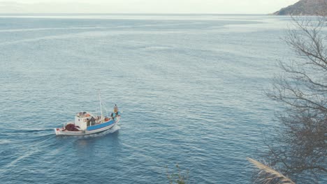 a traditional wooden greek fishing boat driving along the coastline