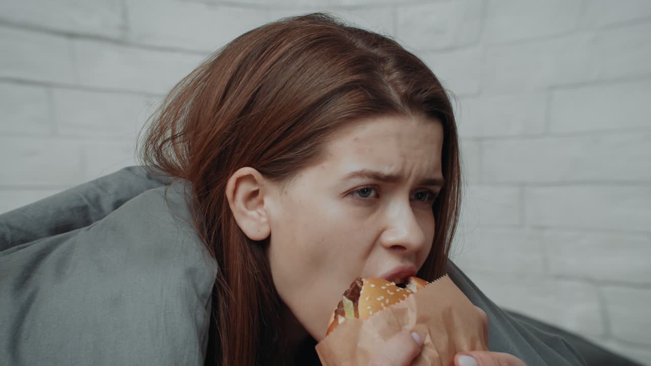 Woman eating a hamburger in bed
