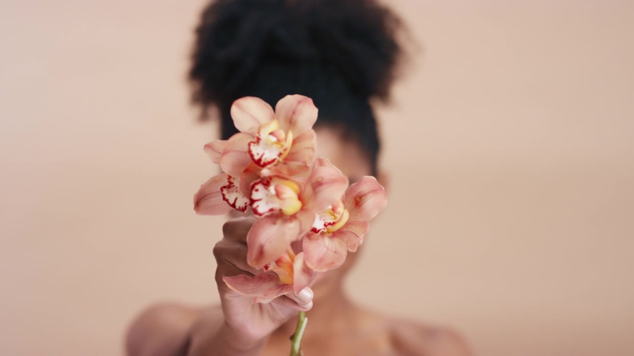Giovane donna che tiene un fiore di orchidea davanti al viso