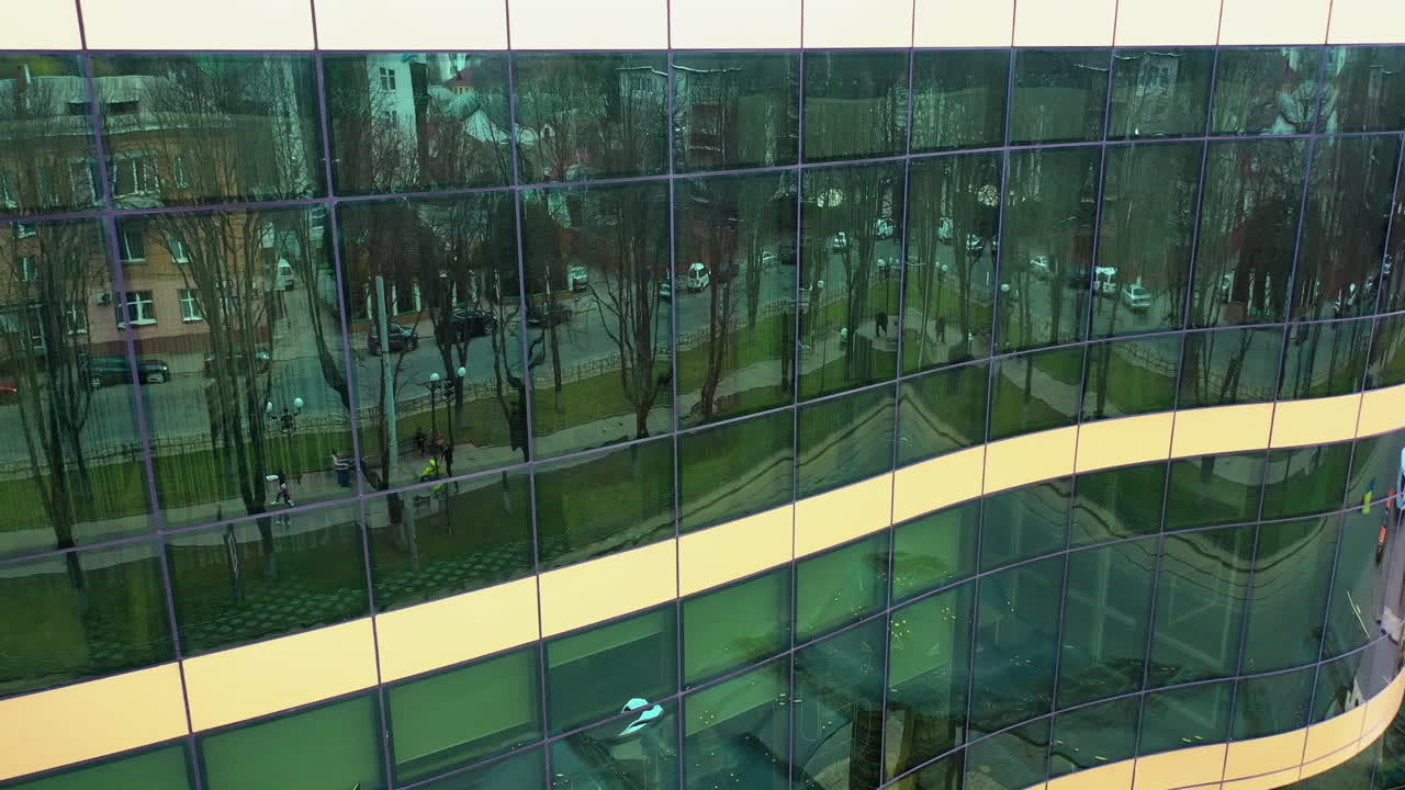 Exterior of the modern glass building reflecting cityscape. Aerial shot of beautiful financial center with reflective glass walls outside. Camera moves top down.