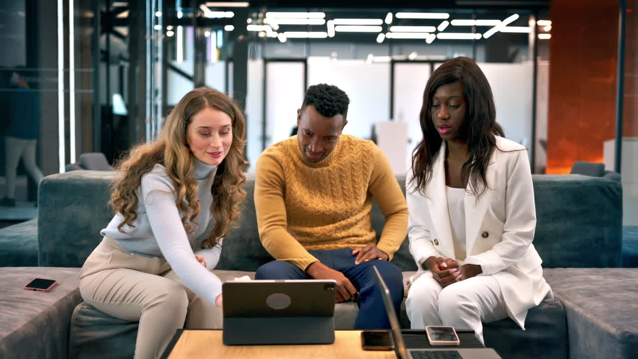 Multiracial group of people in an office discussing business while sitting on a sofa, tablet on the table