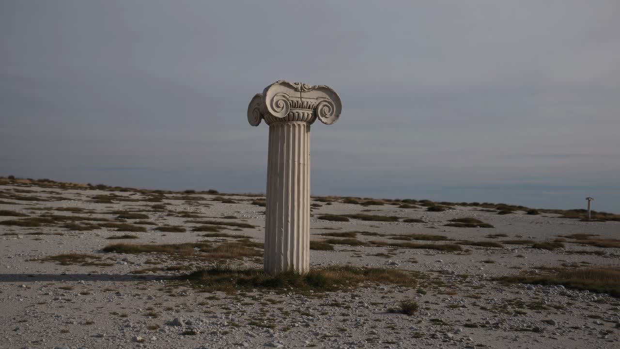 Un'antica colonna solitaria si erge in un paesaggio brullo, catturata da un'angolazione bassa.