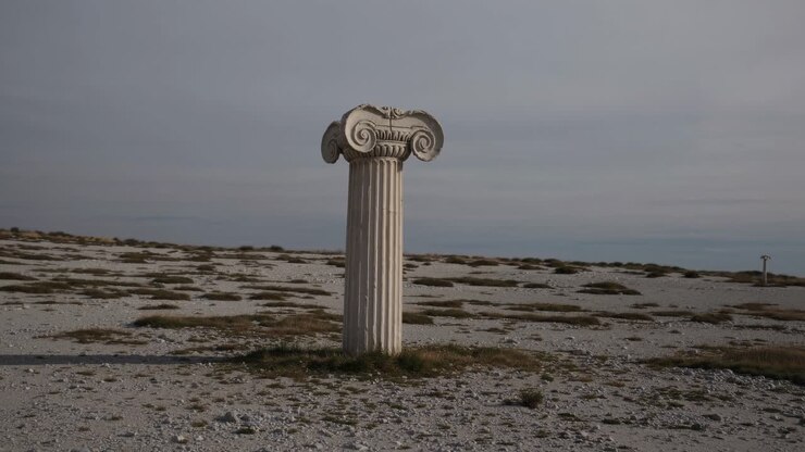 Un'antica colonna solitaria si erge in un paesaggio brullo, catturata da un'angolazione bassa.