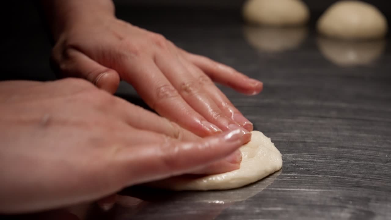 Hands Pressing and Flattening Dough on a Metal Surface
