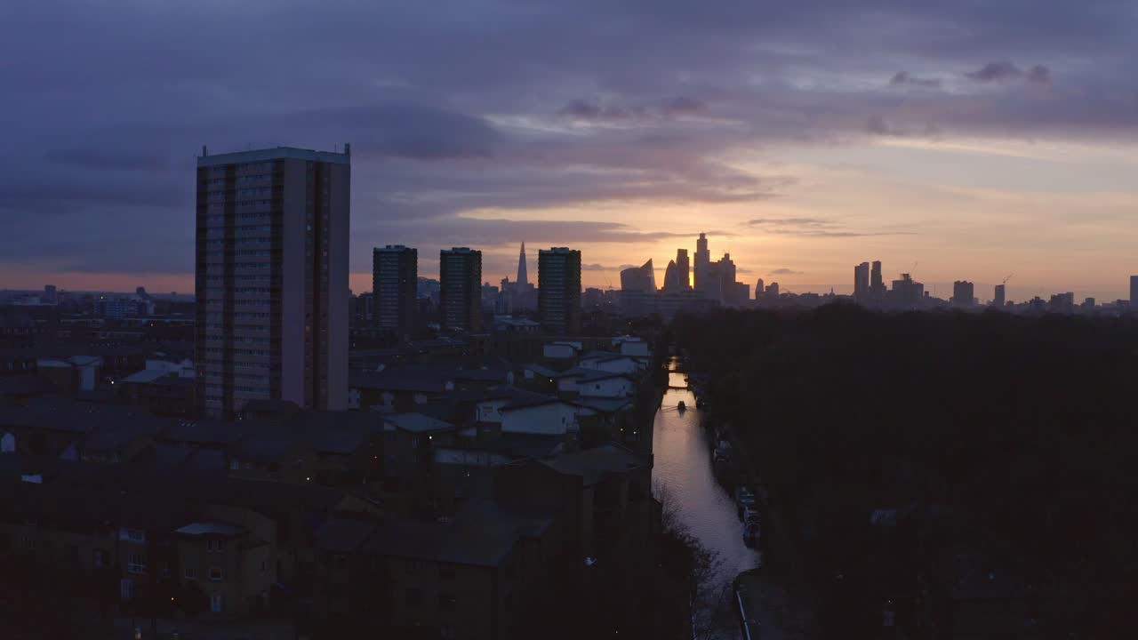 Toma de dron aérea con retroceso de dolly bajo de una casa flotante en el Canal de Londres, parque Victoria, hacia el horizonte de la ciudad y la autopista al atardecer