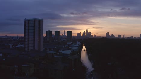 Low-Dolly-Back-Luftdrohnenaufnahme-Des-Hausboots-Auf-Dem-Londoner-Canal-Victoria-Park-In-Richtung-Skyline-Der-Stadt-Zur-Autobahn-Bei-Sonnenuntergang