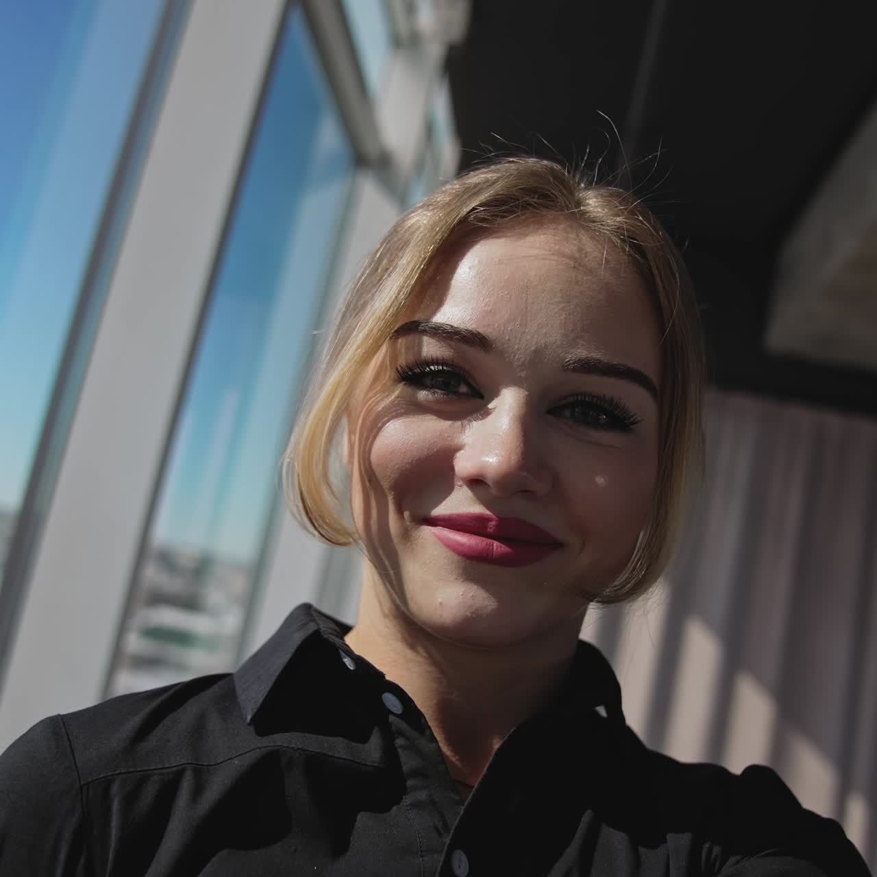 Good-looking young red-haired lady is taking selfie in the light coming from window. Portrait of a beautiful smiling girl inside the building