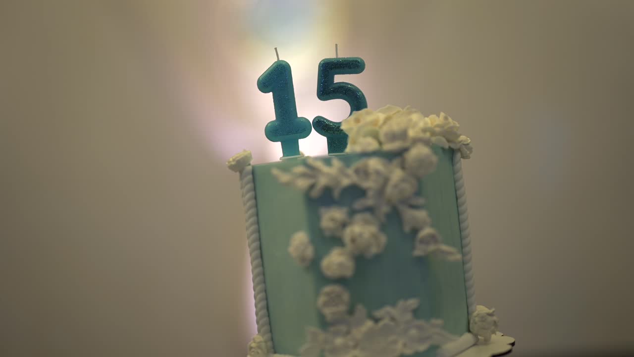 Blue birthday cake with glittery “15” candles and white icing flowers. Soft lighting and shallow depth of field create a dreamy, elegant atmosphere for a Sweet Fifteen celebration
