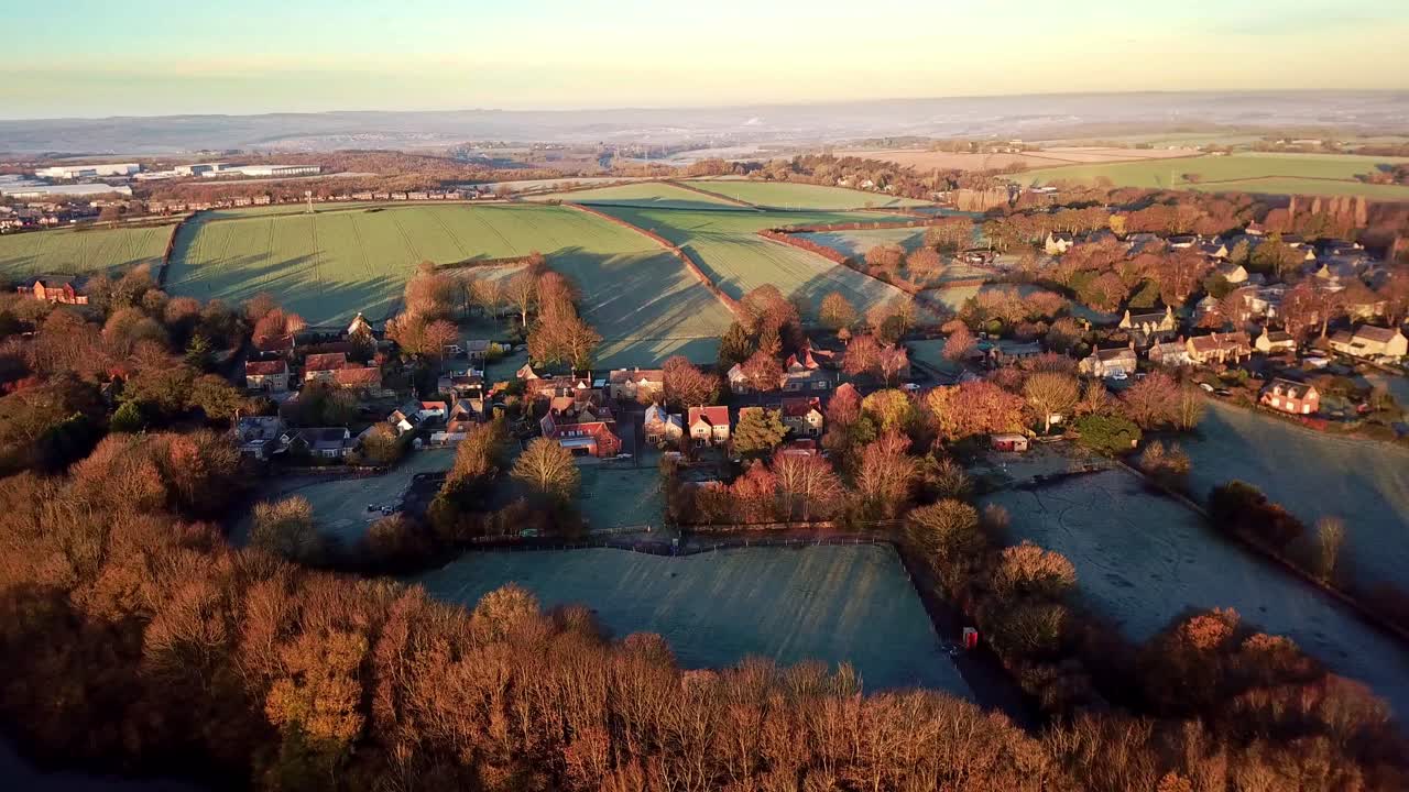 Drone Aerial View Of A Quiet English Village With Rush Hour Traffic Queueing In The Winter With Orange And Brown Trees