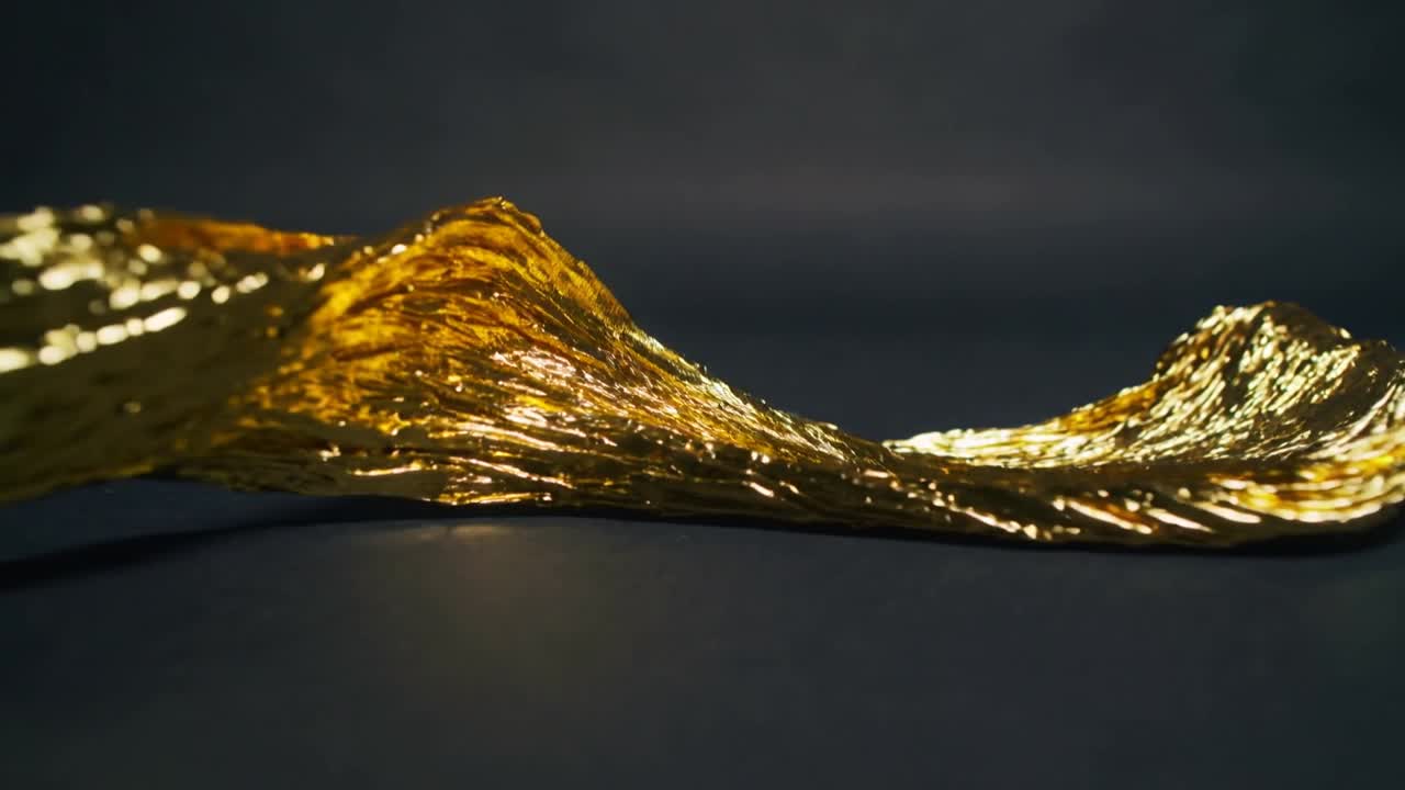 Nastro metallico dorato increspato che si piega e sparge pagliuzze su un tavolo scuro sotto luci da studio.