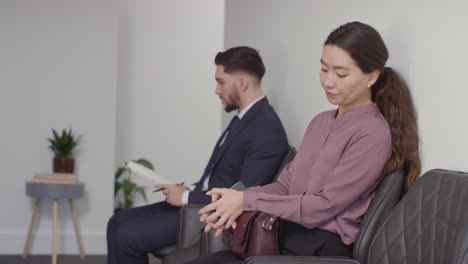 male and female candidates in office waiting for job interview looking at mobile phone and reading notes 5