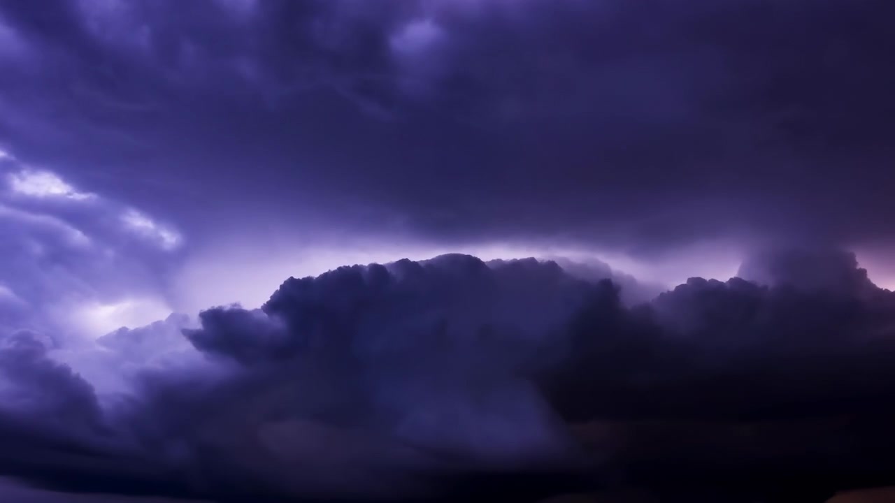 Panoramic purple cumulonimbus cloudscape with dramatic backlit anvil shape, layered towering formations, billowing tops, deep shadows, and glowing storm texture across wide sky