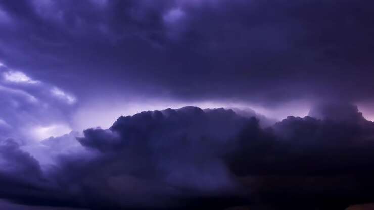 Panoramic purple cumulonimbus cloudscape with dramatic backlit anvil shape, layered towering formations, billowing tops, deep shadows, and glowing storm texture across wide sky