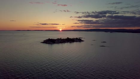 high view of rocky pine tree island in blue lake at sunset, drone aerial wide dolly in