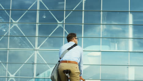 Back-view-of-attractive-man-in-the-casual-style-riding-a-bicycle-close-to-a-glass-building