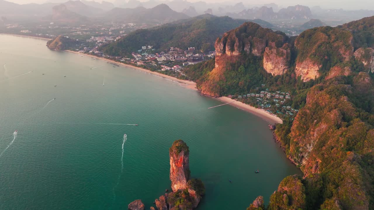 Sweeping aerial panoramic overview of of Krabi Ao Nang Beach with lush cliffs meeting the crystal clear ocean as boats traverse the waters
